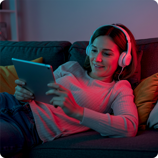 Woman wearing headphones browsing on a tablet on a couch